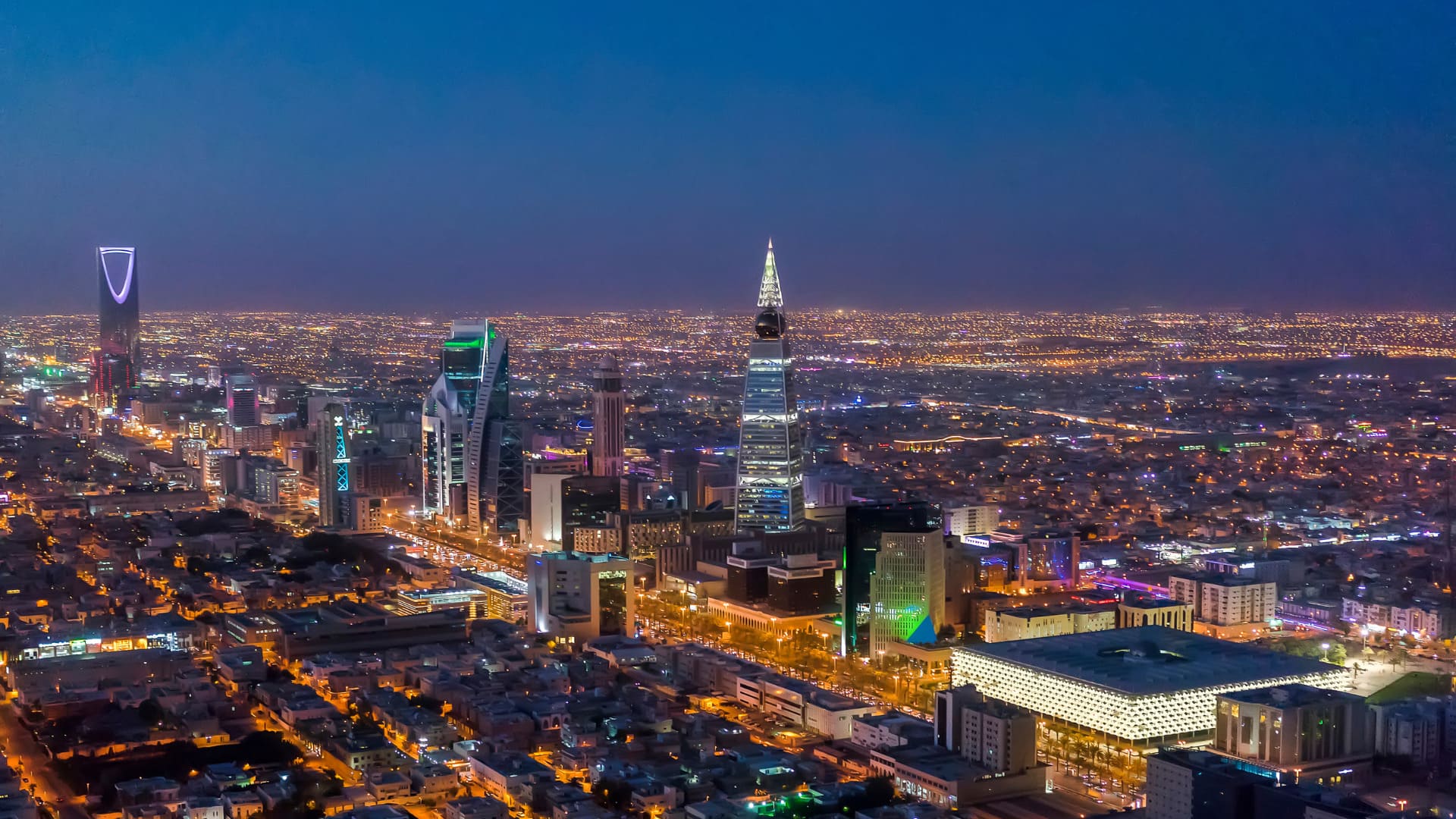 An aerial night view of the Riyadh skyline, showcasing illuminated modern skyscrapers against a backdrop of a vast cityscape. The image represents the advancements in sustainable architecture as part of Saudi Arabia's Mostadam Green Building Certification